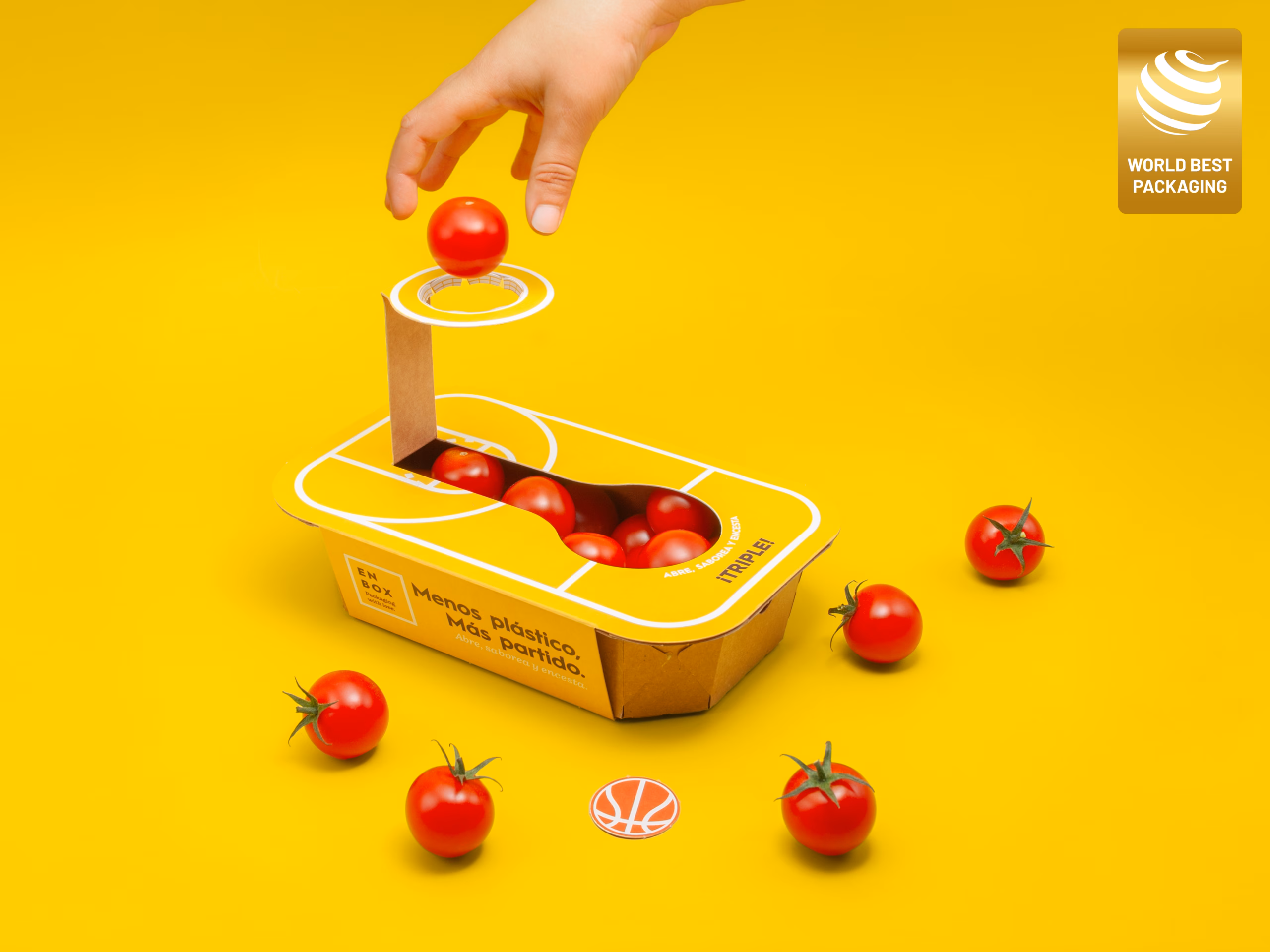 Mano metiendo un tomate cherry por el aro troquelado de cartón de la barqueta ENBOX ganadora del World Best Packaging 2026